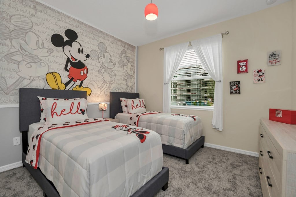 Mickey Mouse-themed guest room with two twin beds, a TV, and access to a shared bathroom.