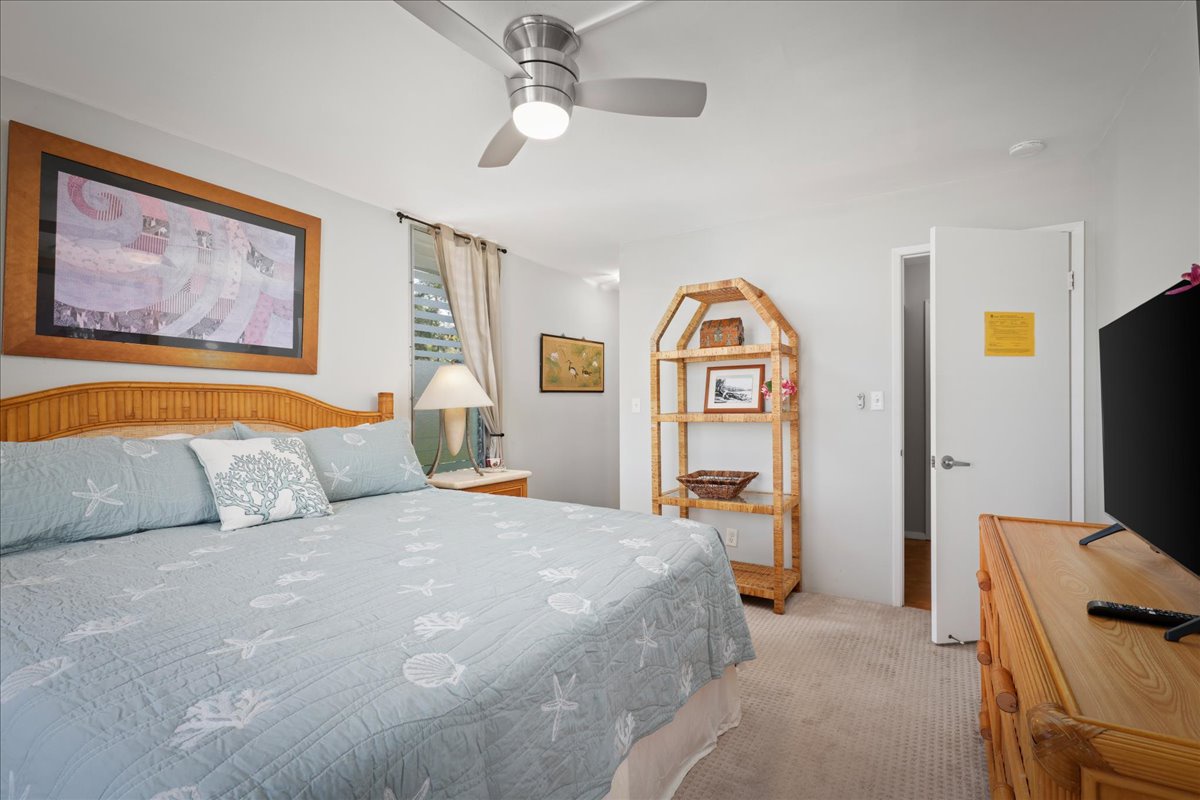 Relax in this breezy bedroom featuring a king-size bed with coastal bedding, rattan furnishings, and a ceiling fan for comfort.