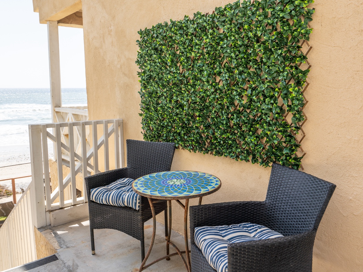 Ocean-view balcony with wicker chairs and mosaic bistro table at