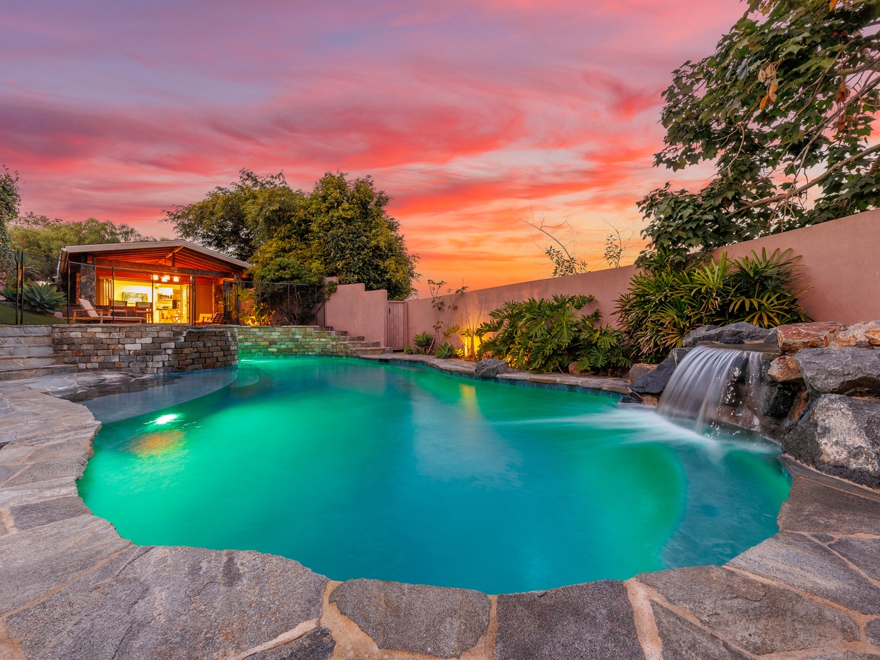 Resort-style swimming pool with stone waterfall and sunset views