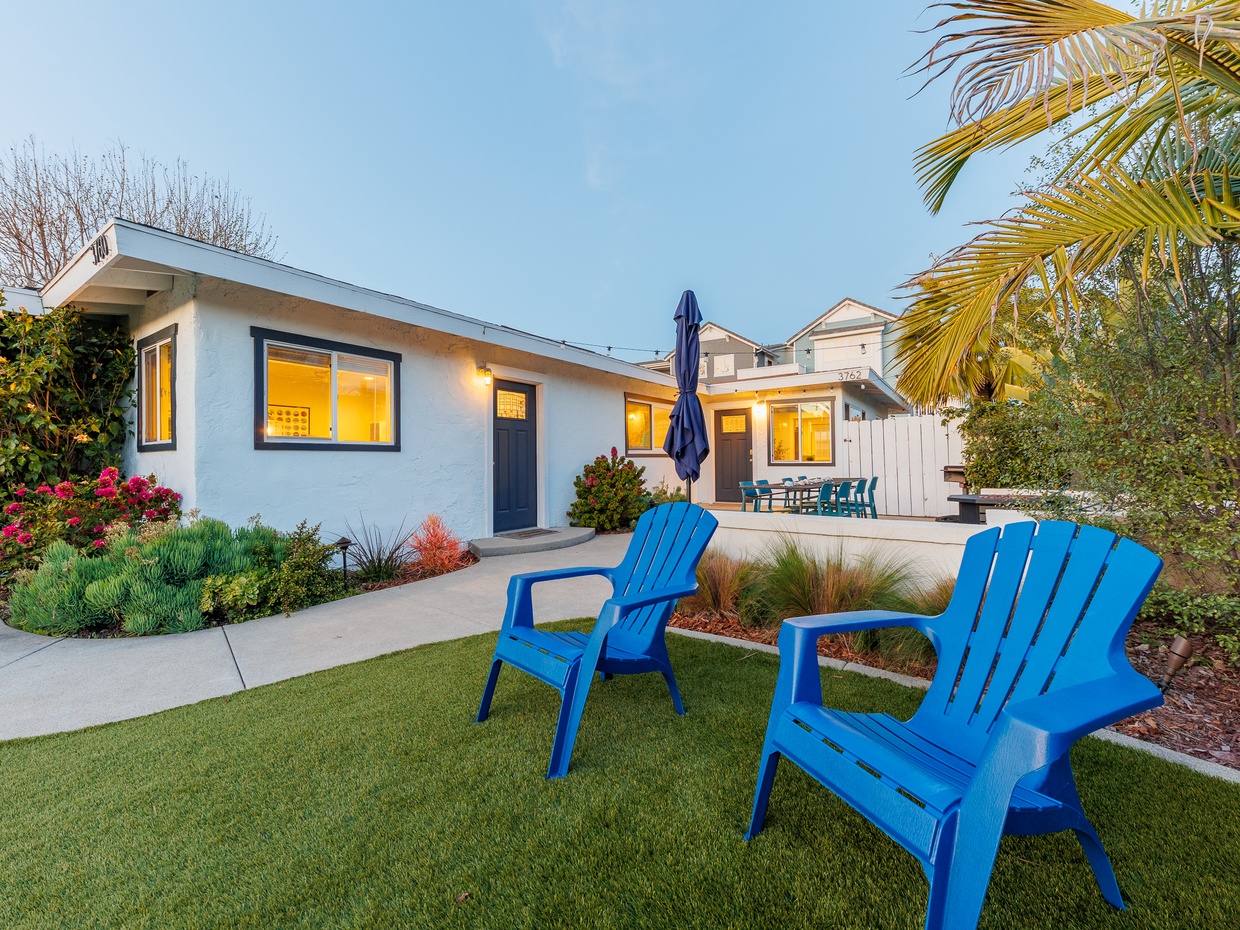 Grassy backyard with blue Adirondack chairs and tropical landsca