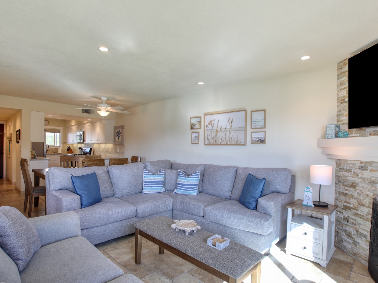 The open-concept living area features comfy seating, a cozy fireplace, and large windows that let in the ocean breeze and natural light.