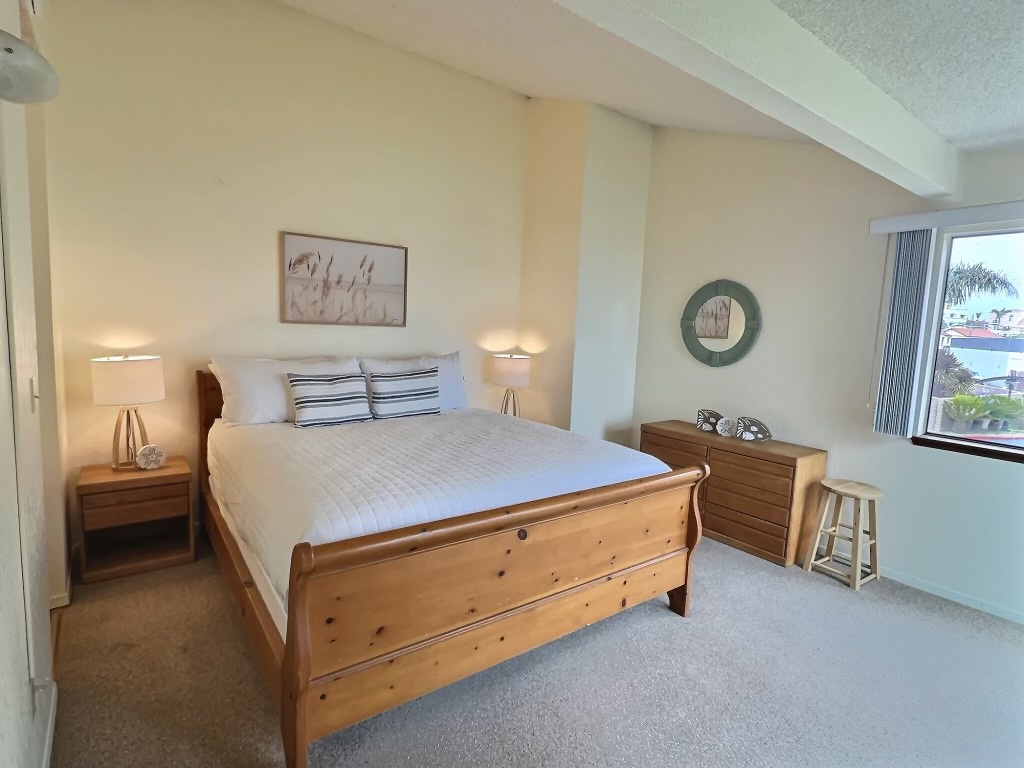 The master suite features a luxurious king bed, a private bathroom vanity, and a charming peek-a-boo view of the ocean. The shower area is 'shared' with bedroom 2. 