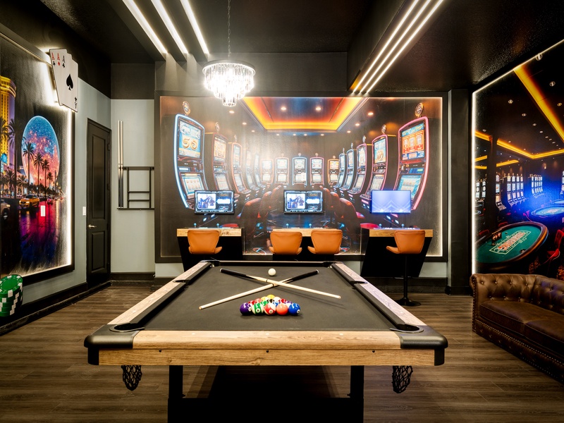 A one-of-a-kind Vegas-style game room featuring a pool table, bar seating, PS5 gaming stations, arcade stations and stunning floor-to-ceiling casino artwork.