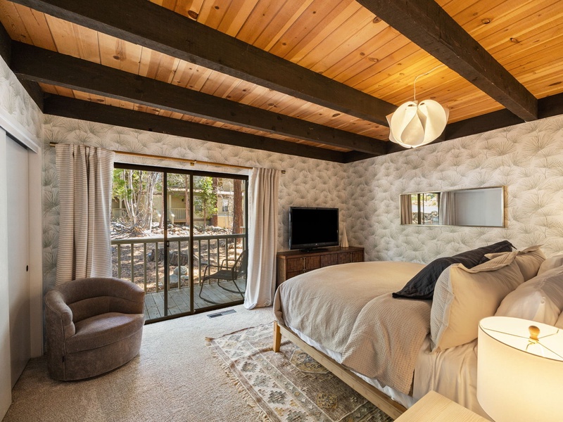 An alternate view of Bedroom #1 with a reading chair, TV, and private balcony