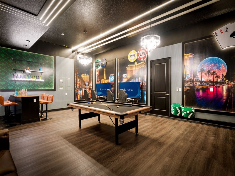 A one-of-a-kind Vegas-style game room featuring a pool table, bar seating, PS5 gaming stations, and stunning floor-to-ceiling casino artwork.