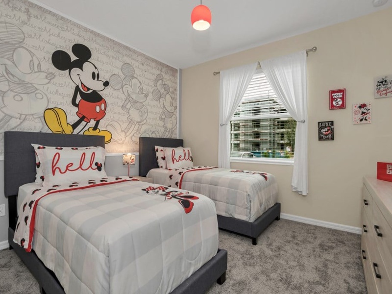 Mickey Mouse-themed guest room with two twin beds, a TV, and access to a shared bathroom.