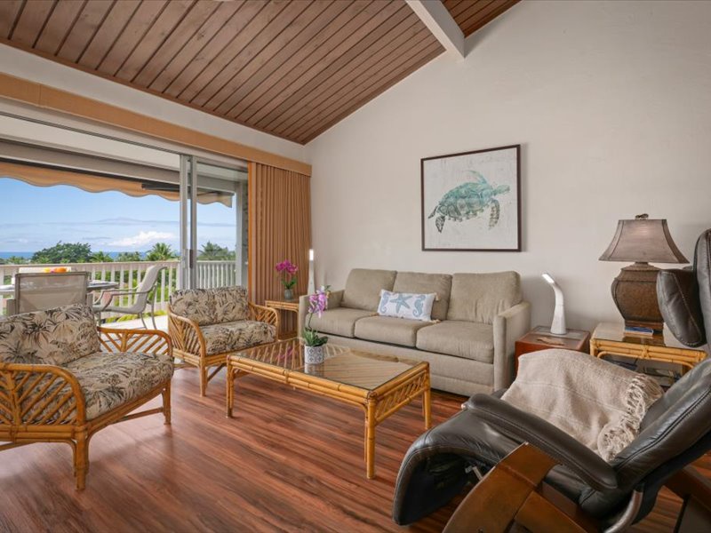 This inviting living room features vaulted wood ceilings, warm island-inspired furnishings, and a seamless connection to the ocean-view lanai