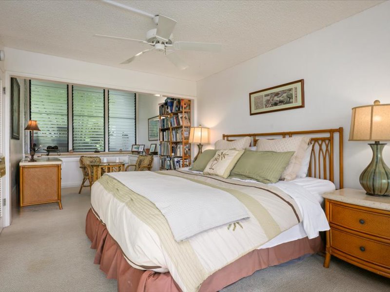Relax and unwind in the spacious primary bedroom featuring a plush king bed, warm natural tones, and a private lanai surrounded by tropical greenery.