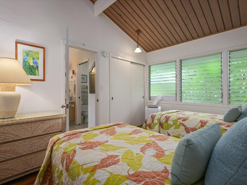 This inviting guest bedroom features two cozy twin beds, a vaulted wood ceiling, and easy access to the adjoining bathroom