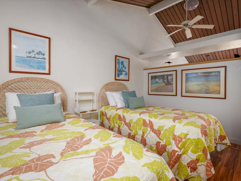 This bright upstairs guest bedroom features two comfortable twin beds, a vaulted ceiling with cooling fan, A/C, and cheerful island-inspired décor