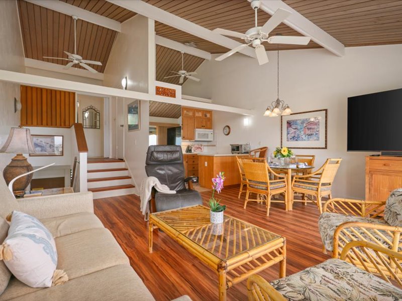 This bright, airy living space features vaulted ceilings, tropical furnishings, and an open layout that connects the kitchen, dining, and lanai areas