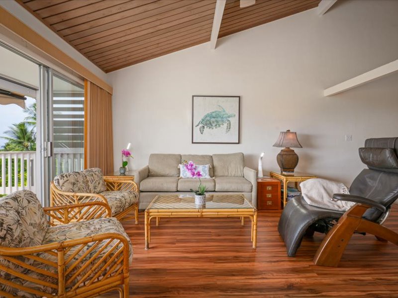 Relax in this bright, inviting living room featuring vaulted ceilings, warm wood floors, and tropical-style furniture