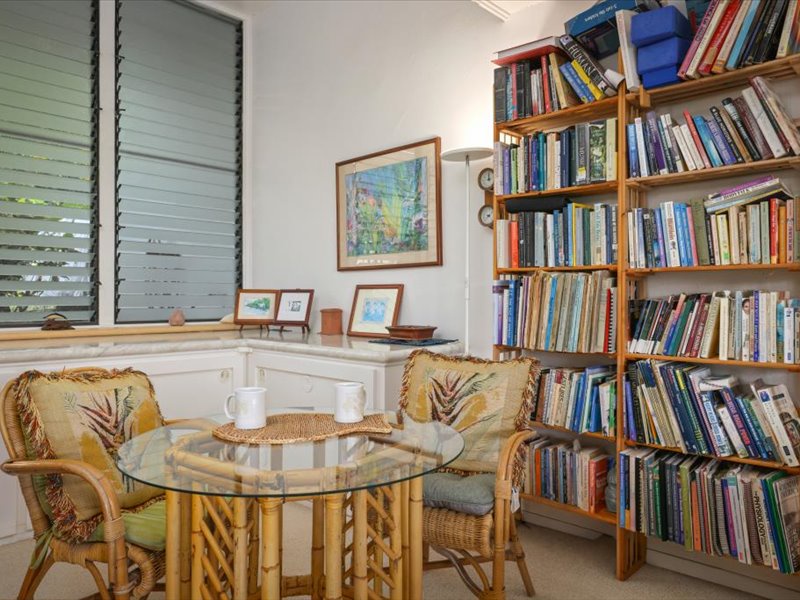 This inviting reading nook features a wall of books, tropical artwork, and a glass-top table with rattan chairs
