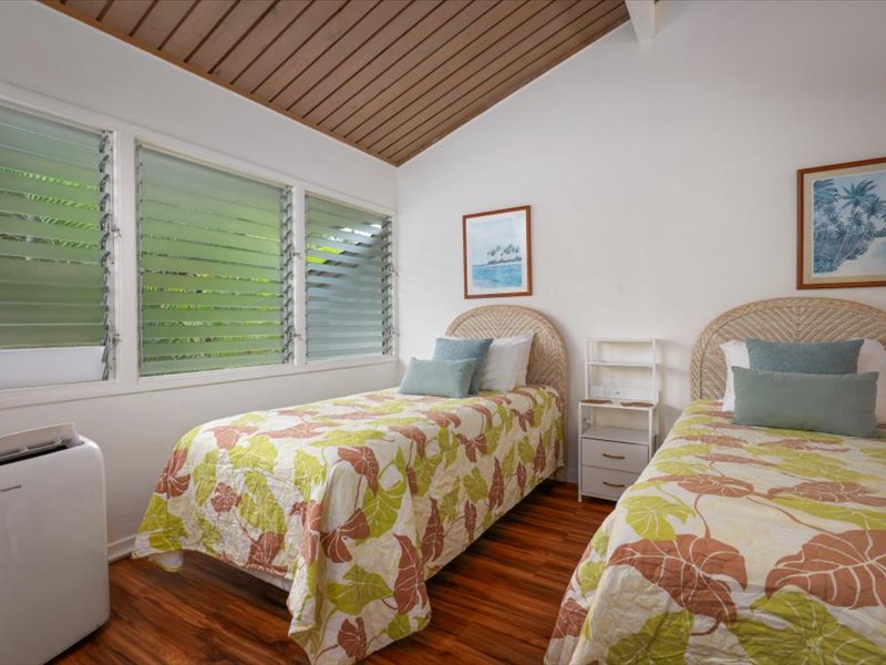 This cheerful guest bedroom features two comfortable twin beds, vaulted ceilings, and rich wood floors for a warm island feel.