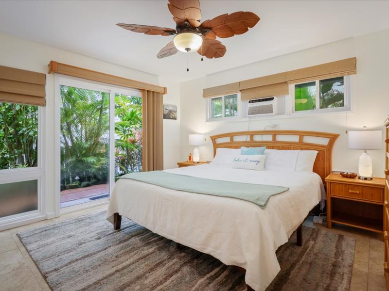 Serene bedroom with a king bed, tropical furnishings, and sliding doors that open to a lush private lanai.