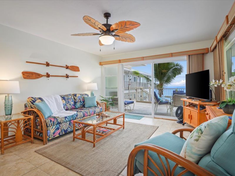Bright ocean-view living room with tropical décor, comfortable seating, and direct access to the lanai overlooking the Kona Coast.