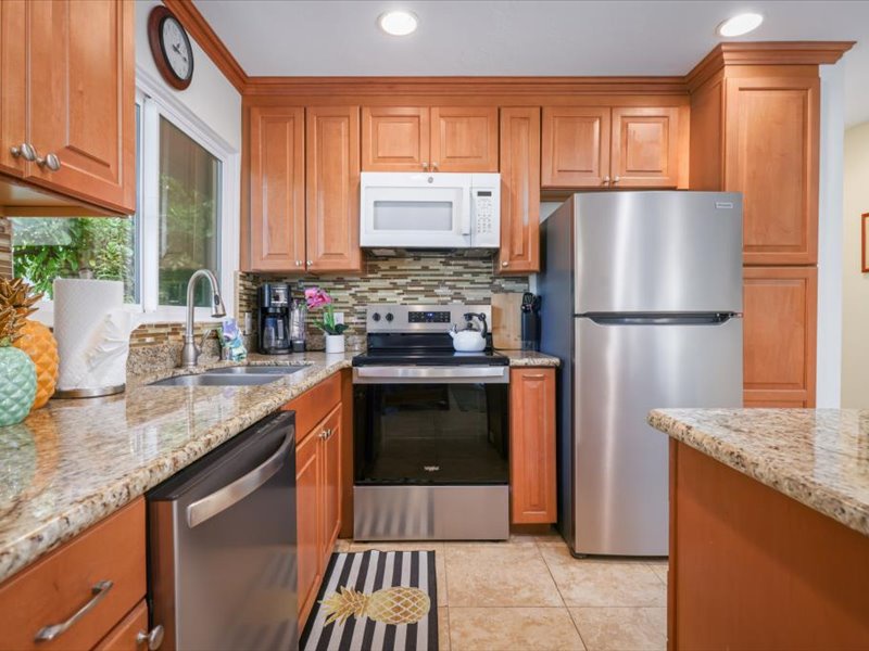 Contemporary kitchen featuring stainless steel appliances, granite countertops, and warm wood cabinetry with tropical accents.