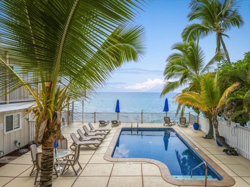 Oceanfront pool area surrounded by swaying palms and lounge chairs, offering the perfect spot to relax and take in stunning Kona Coast views.