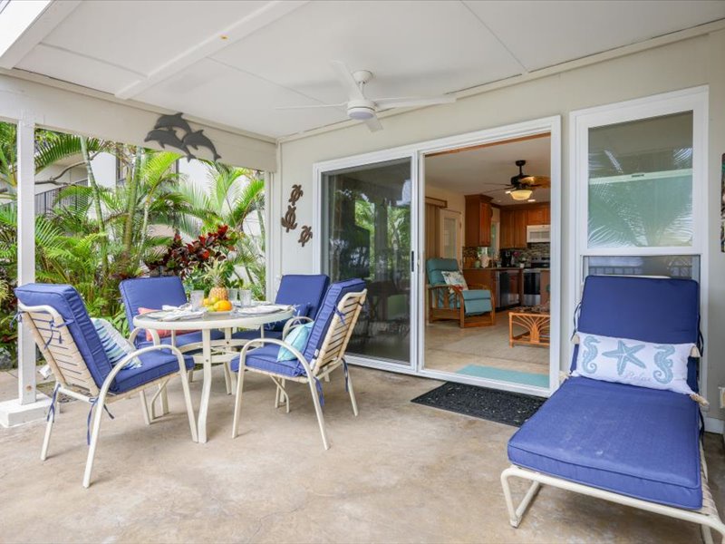 Spacious covered lanai with comfortable seating and lounge chairs, perfect for outdoor dining and relaxing in the tropical breeze.