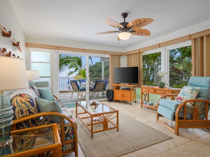 Bright and airy living room with tropical décor, comfortable seating, and stunning ocean views through large windows and sliding doors.