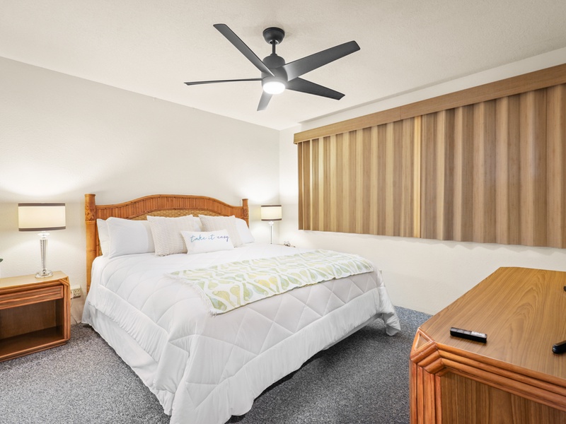 Unwind in this serene primary bedroom featuring a plush king bed, island-style furnishings, soft lighting, and custom window treatments—perfect for restful nights and lazy mornings