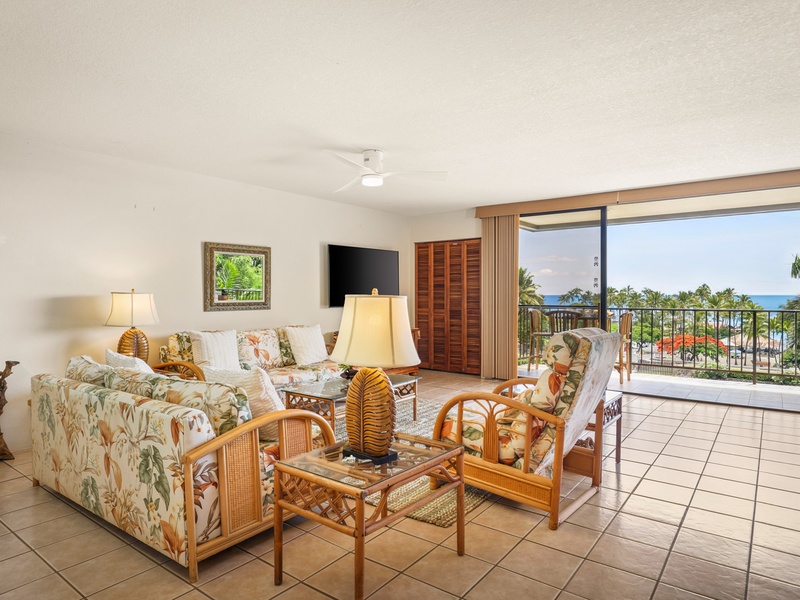 Spacious living area with tropical furnishings opens to a large lanai overlooking the ocean—perfect for relaxing or entertaining in island style
