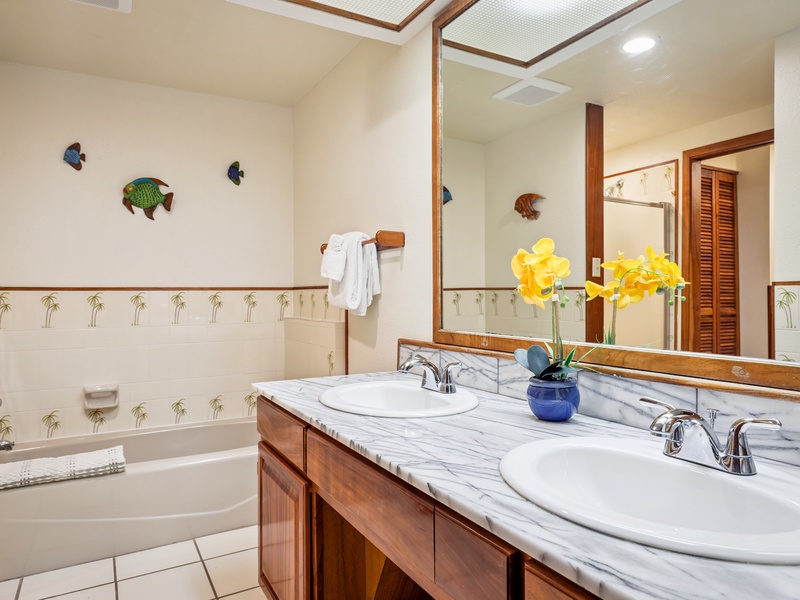 This bright and roomy primary bathroom features a double vanity with marble countertops, a full size tub, walk in shower, and playful palm tree tile accents—perfect for relaxing after beach days