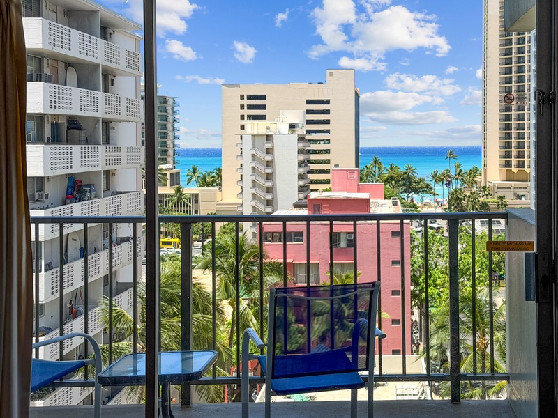 Step onto the private lanai/balcony at Waikiki Park Heights #808, settle into the outdoor seating, and enjoy warm island light with palm-lined city scenery and a refreshing partial Pacific Ocean view.