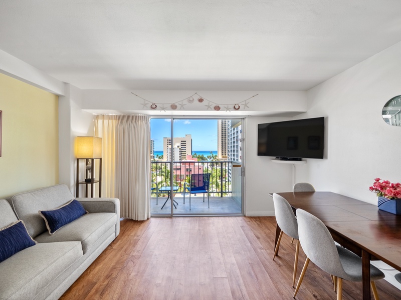 Gather in a bright, easygoing living and dining space where the sofa, four-seat table, and open lanai/balcony share a partial Pacific view. It’s an inviting Waikiki home base for relaxing, dining, or working.