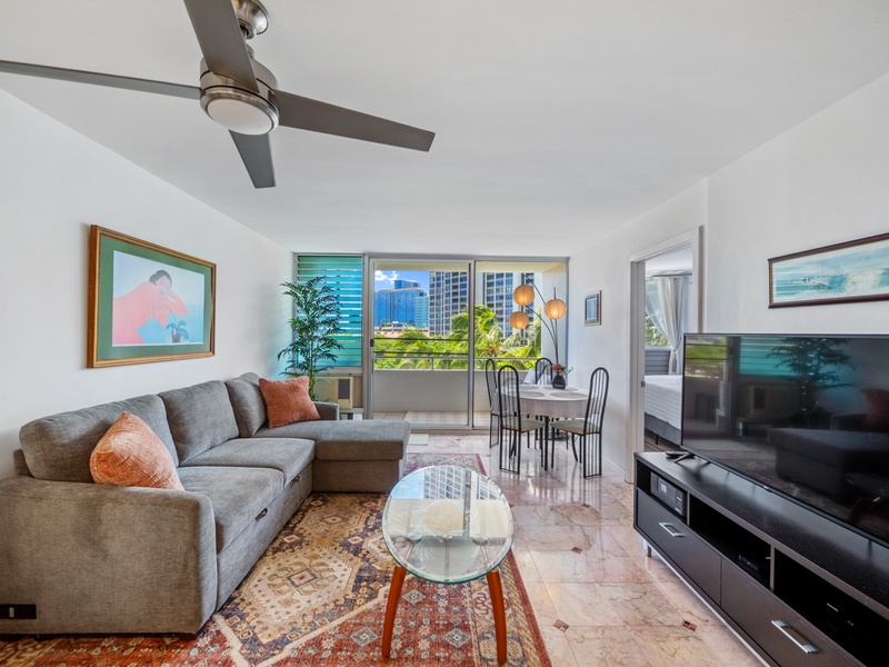 Welcome to Harbor View Plaza #409, a bright two-bedroom Waikiki monthly rental with a comfortable sectional, 65-inch Smart TV, dining area, and private lanai/balcony framed by palms and city views.