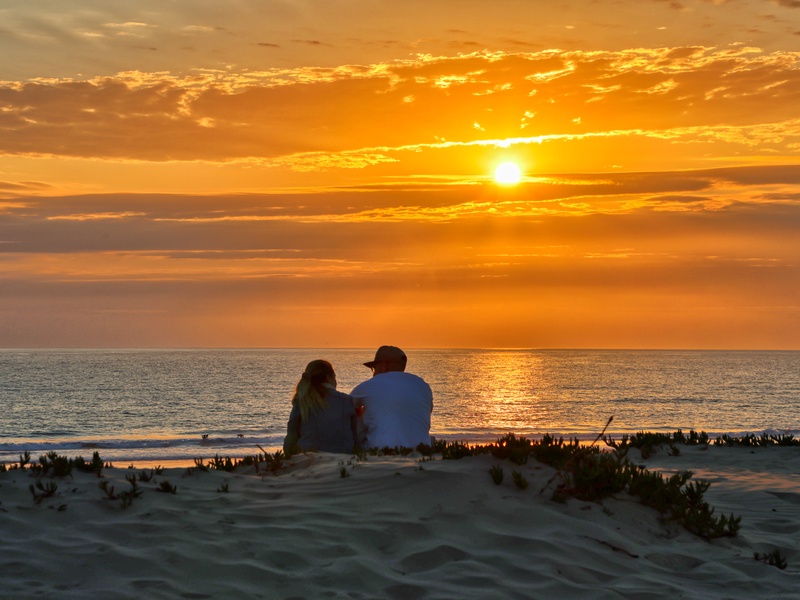 Watching the sun dip below the horizon, a young couple relaxes on the sand in the Oceano Dunes.
