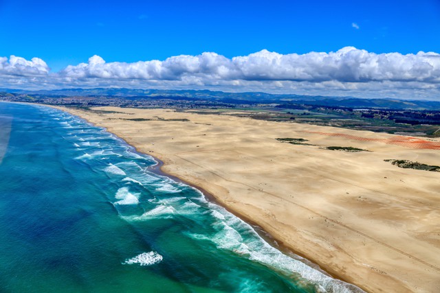 An aerial view of the Oceano Dunes coastline, where the rolling sand dunes meet the sparkling waters of the Pacific Ocean.
