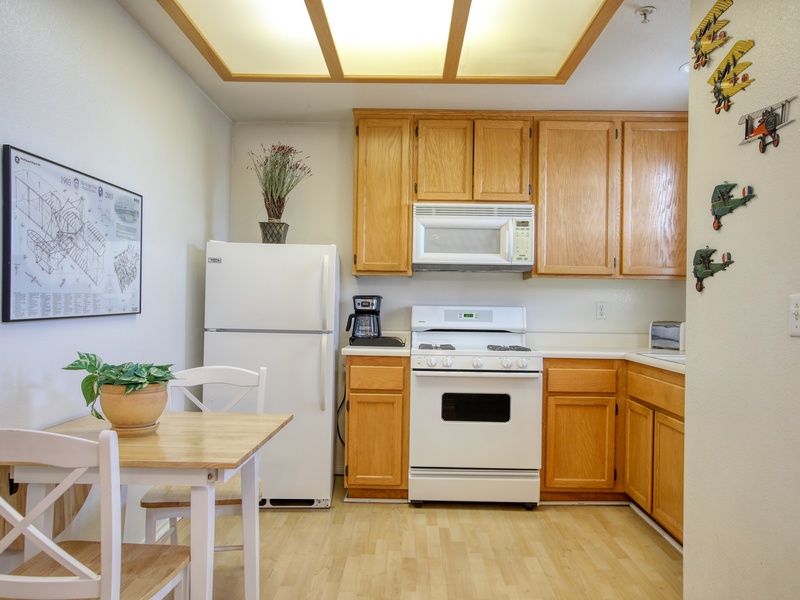 This cozy kitchen features warm wood cabinetry, a full-size refrigerator, gas stove, microwave, and a quaint dining nook, perfect for enjoying meals in a bright, inviting space.