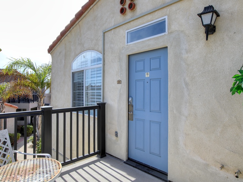 This charming second-floor entry features a soft blue door opening onto a private balcony, perfect for a morning coffee in a tranquil coastal setting.