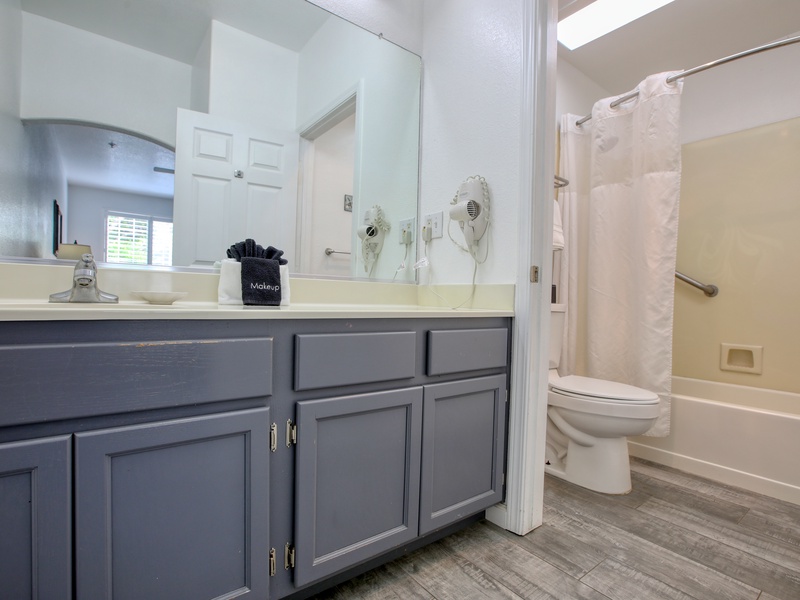 This bathroom features a spacious vanity with ample storage, a large mirror, and a shower-tub combination for convenience.
