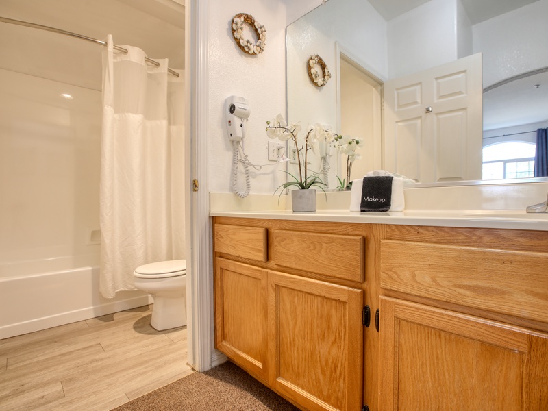 This bathroom features a spacious vanity with ample storage, a large mirror, and a shower-tub combination for convenience.