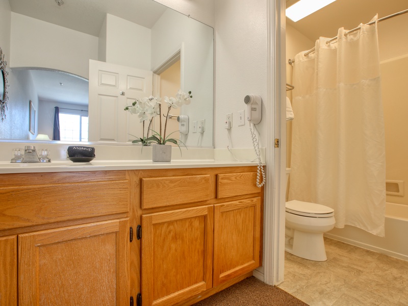 This bathroom features a spacious vanity with ample storage, a large mirror, and a shower-tub combination for convenience.