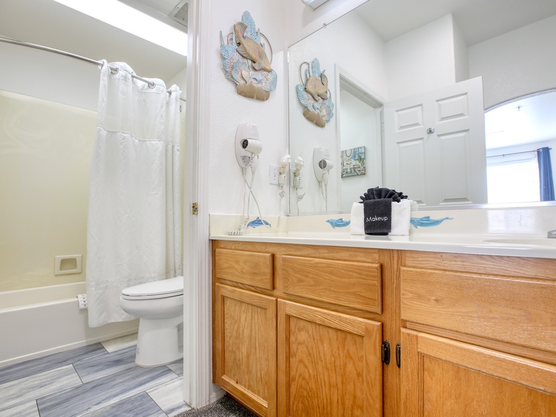 This bathroom features a spacious vanity with ample storage, a large mirror, updated flooring and a shower-tub combination for convenience.