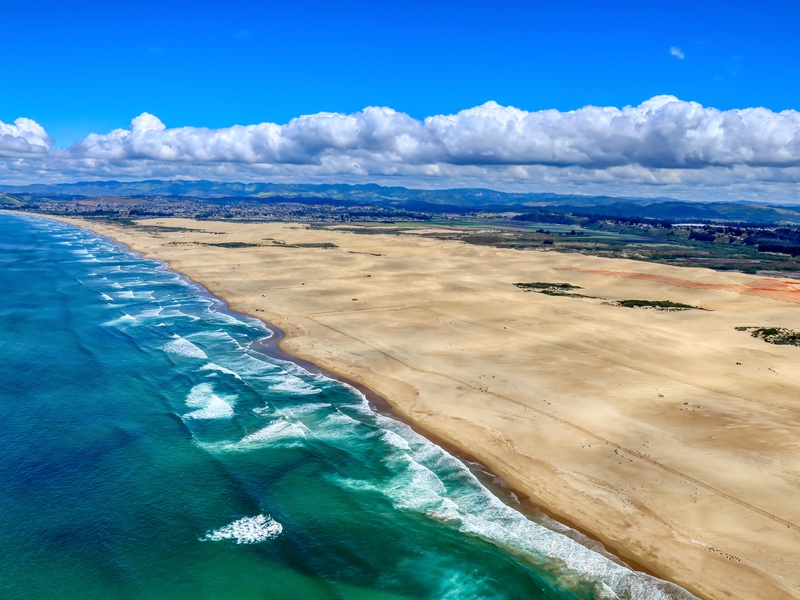 An aerial view of the Oceano Dunes coastline, where the rolling sand dunes meet the sparkling waters of the Pacific Ocean.