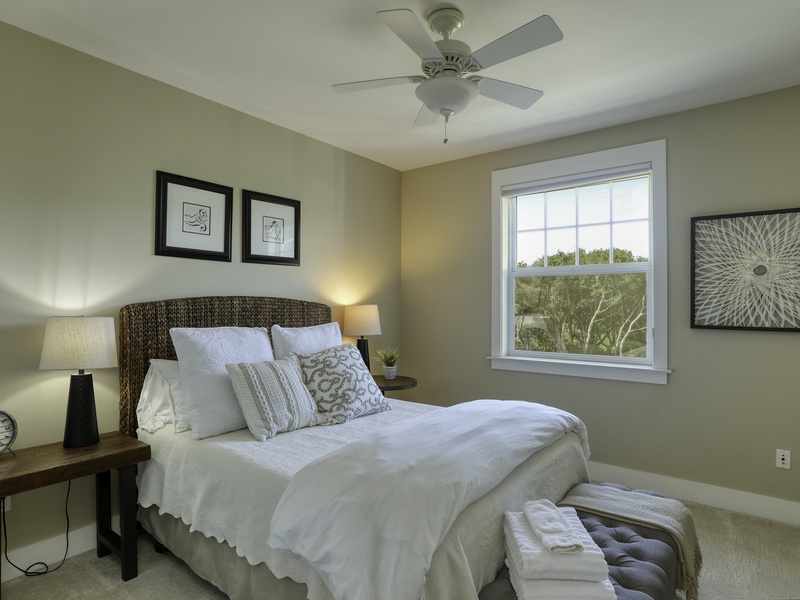 Queen Comfort: Enjoy peaceful rest in this second-level bedroom, featuring a charming woven grass headboard and cozy Queen mattress with white fluffy linens. A full bathroom is conveniently situated nearby for guest use.