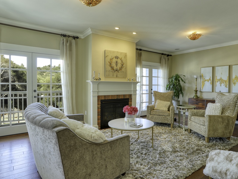 The formal living room, located off the foyer, is an elegant retreat. It boasts plush, luxe furnishings, a charming fireplace, and twin French doors that flood the room with light and open up to the fresh air and views.